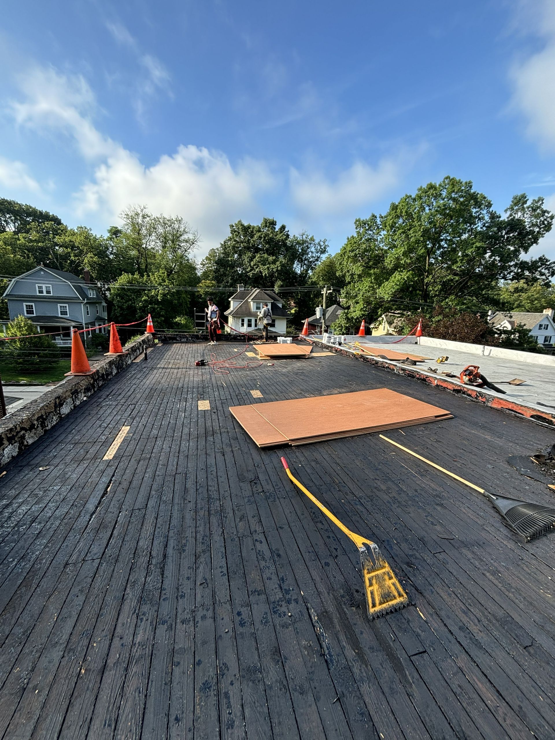 Road under construction with fresh asphalt, orange cones, and workers under a blue sky.