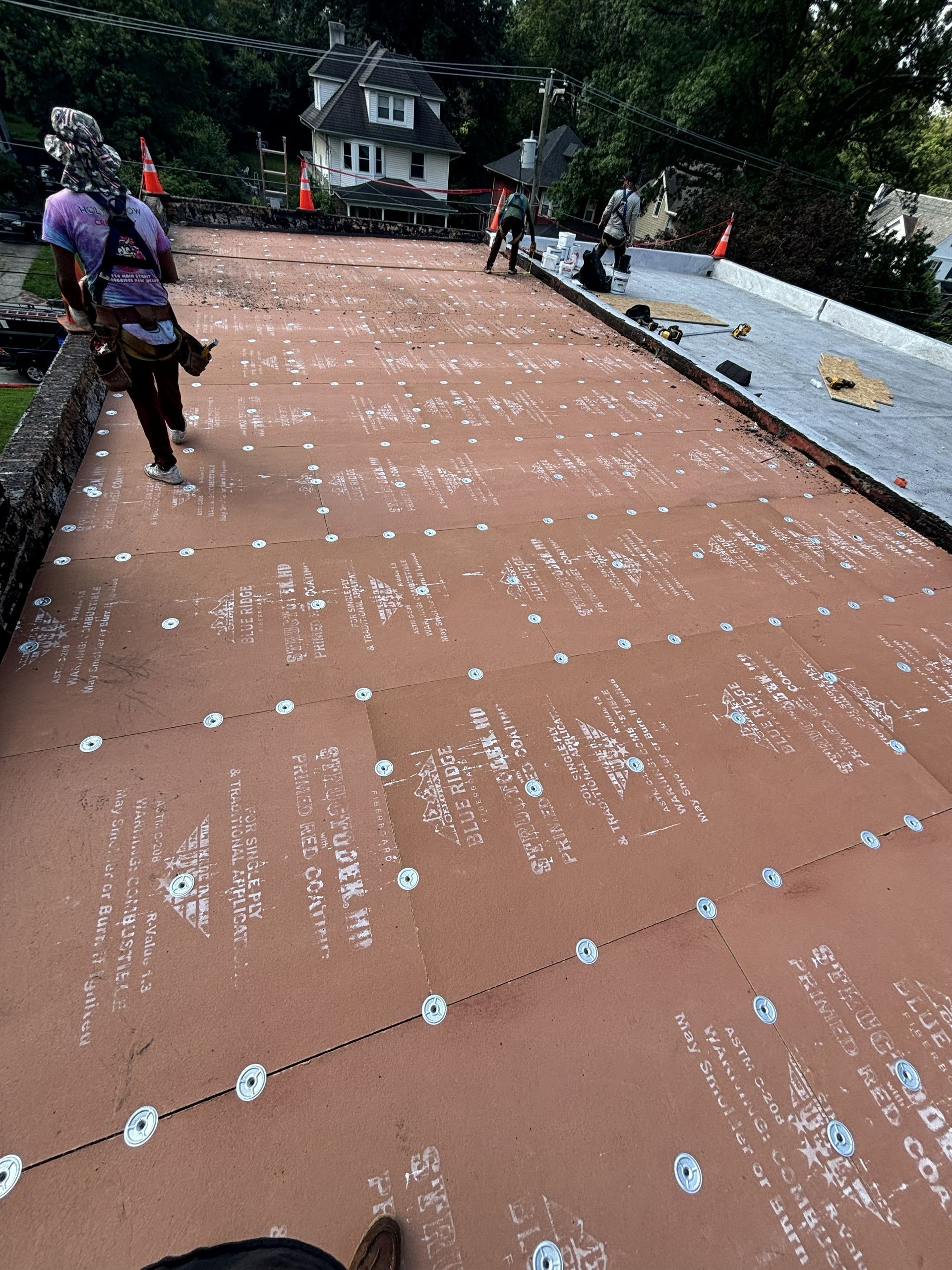 Workers on a rooftop covered in white markers, with a house and trees in the background.