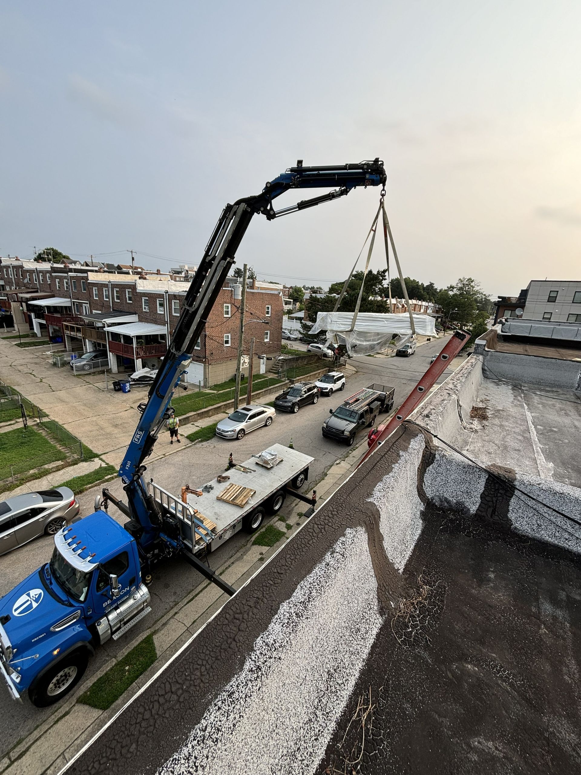 Crane truck lifting a long beam over a construction site beside residential buildings.