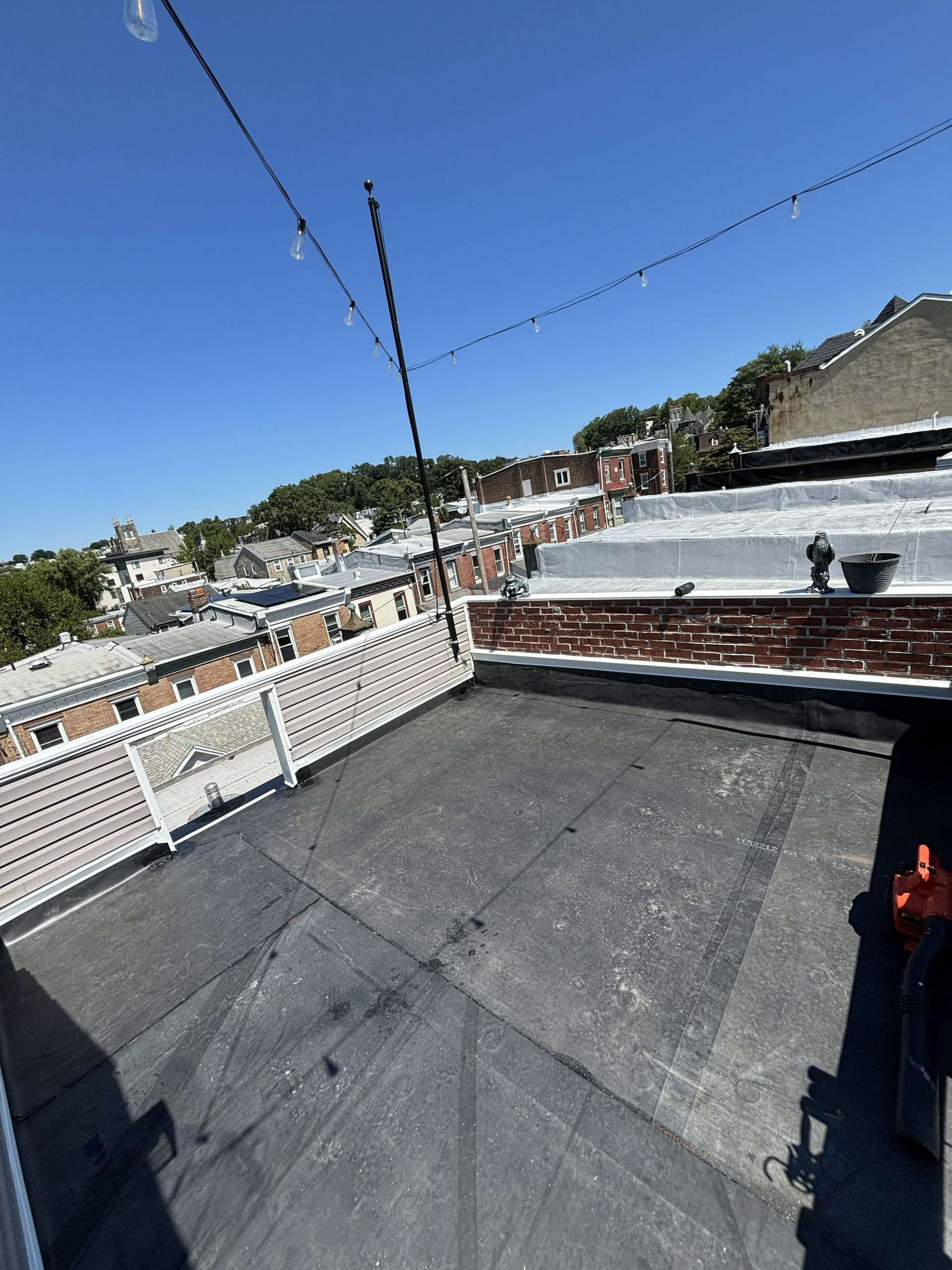 Rooftop deck with white railing, rooftop strings, and a view of houses under a clear blue sky