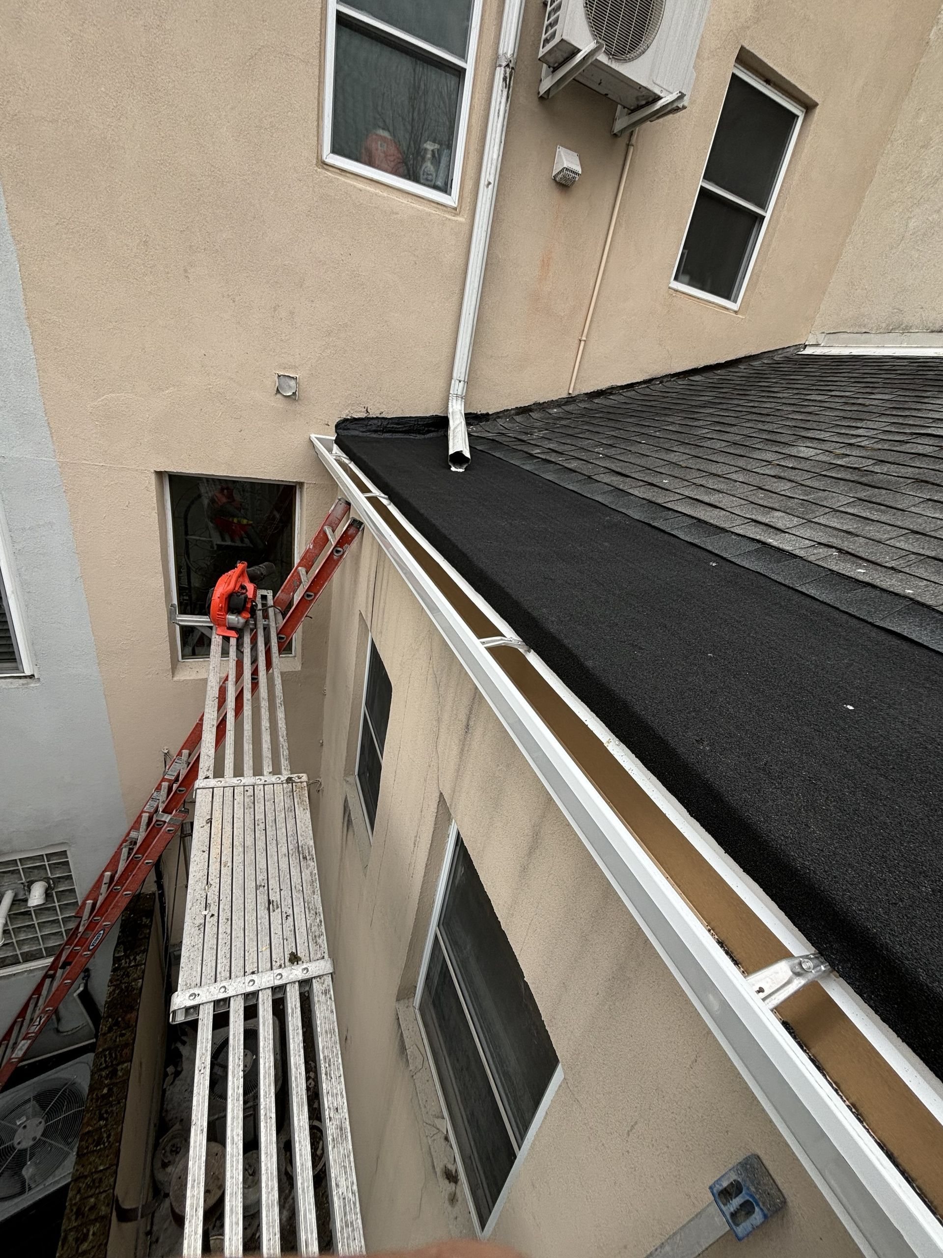 Exterior view of a building’s narrow balcony and stairway with red railing and black roof shingles