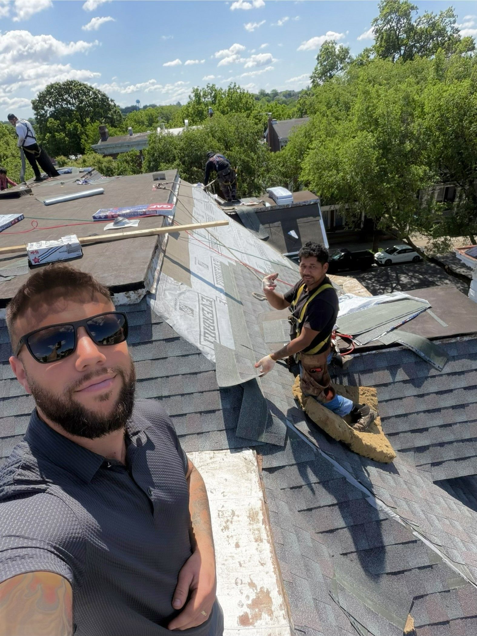 Two workers repairing a rooftop in bright sunlight, with debris and trees in the background.