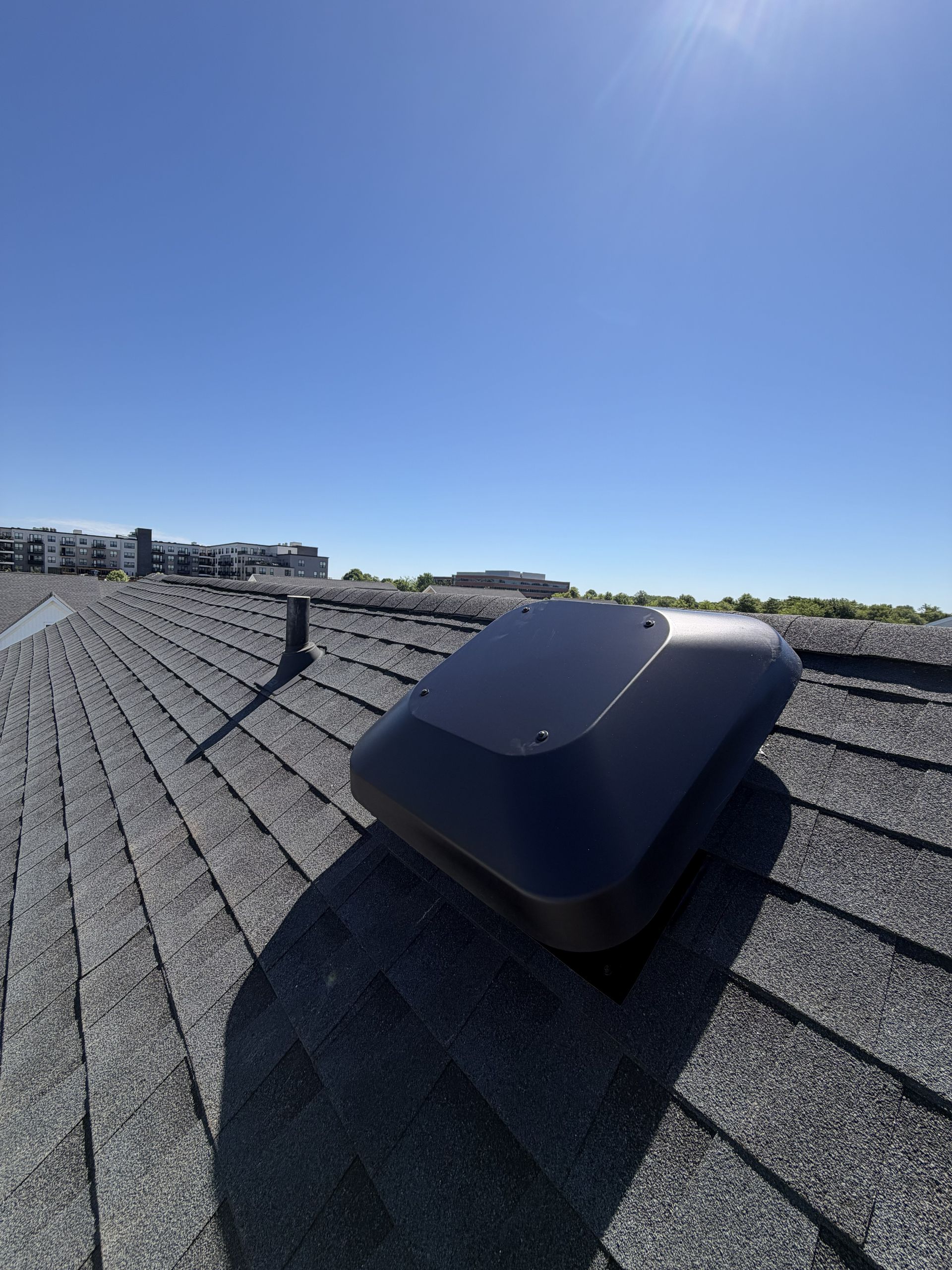 Black roof vent on a shingled rooftop under a clear blue sky
