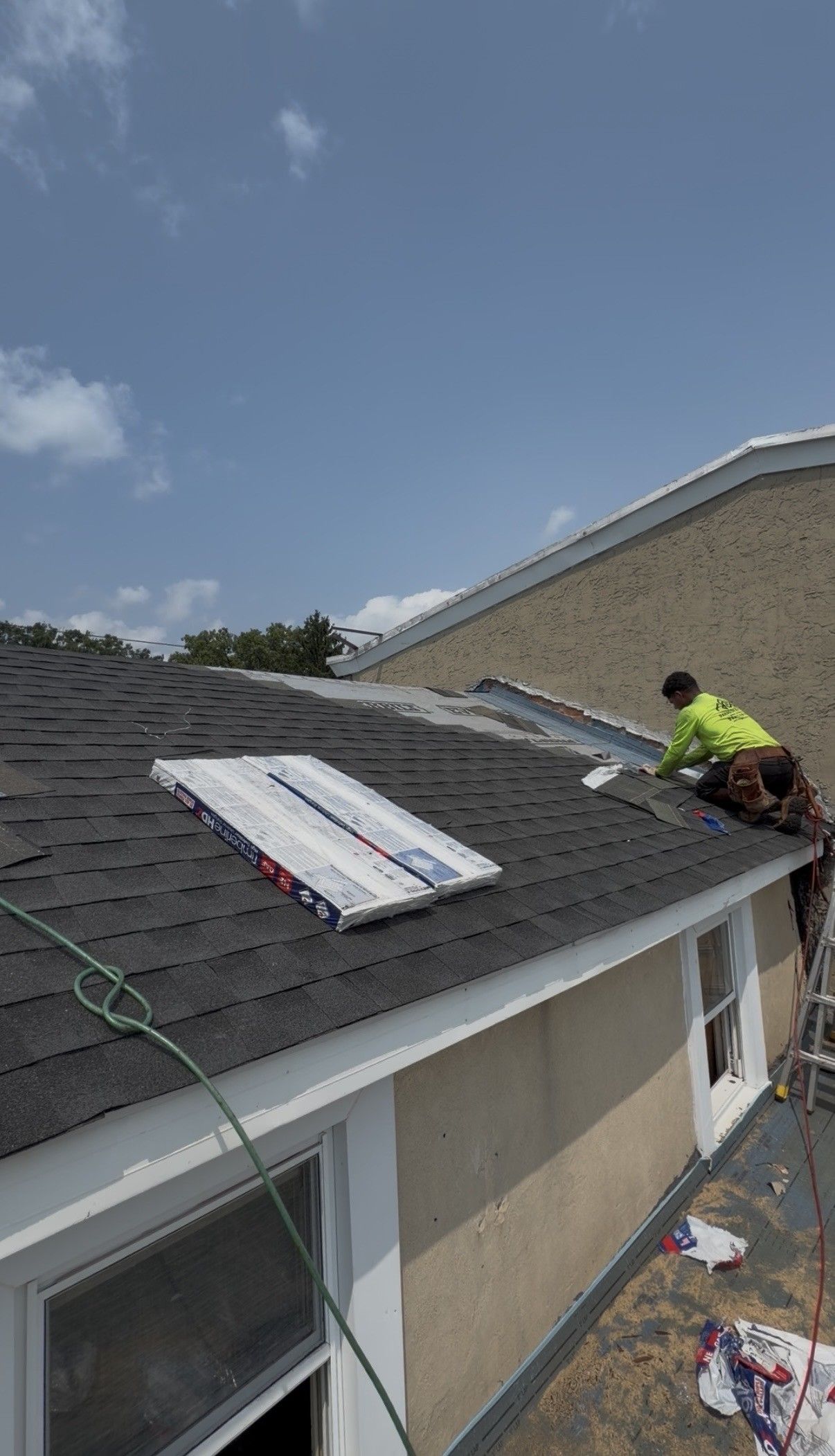 Worker on a roof installing shingles and underlayment on a house roof.