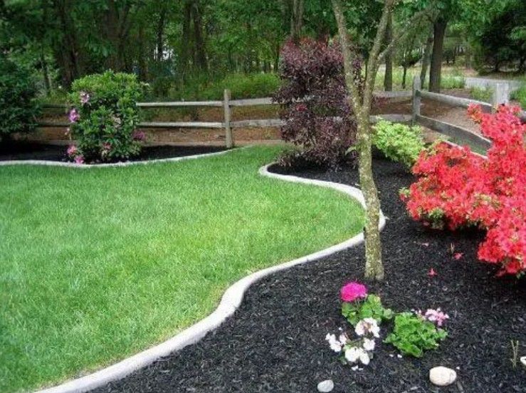 A manicured lawn with a curved concrete border separating it from a black-mulched garden bed with shrubs and red flowers.