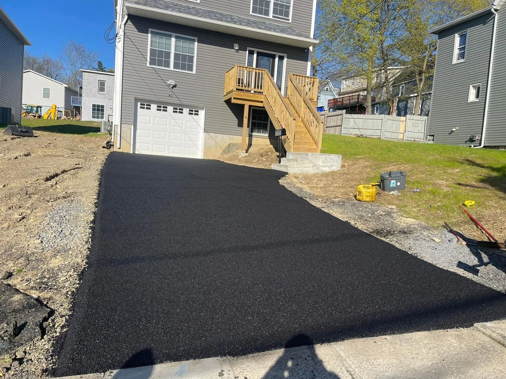 A newly paved black asphalt driveway leads to a gray suburban house with wooden stairs.