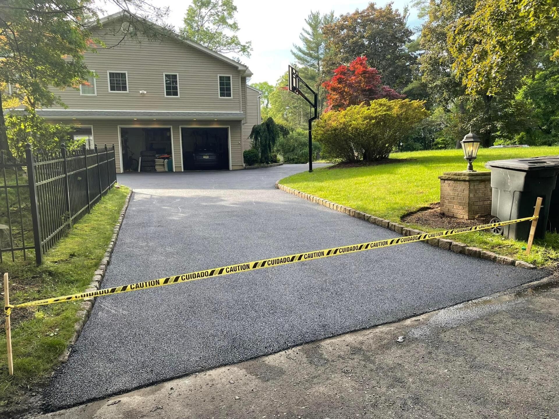 A freshly paved asphalt driveway leading to a two-car garage, blocked by yellow caution tape.