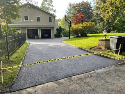 A freshly paved asphalt driveway leading to a two-car garage, blocked by yellow caution tape.