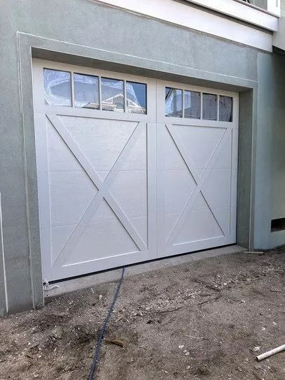 White garage door with window panel above, X-shaped accents, set in a light gray wall.