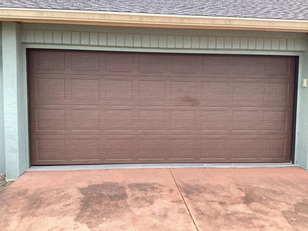 Brown garage door on a house with light green walls and a brown concrete driveway.