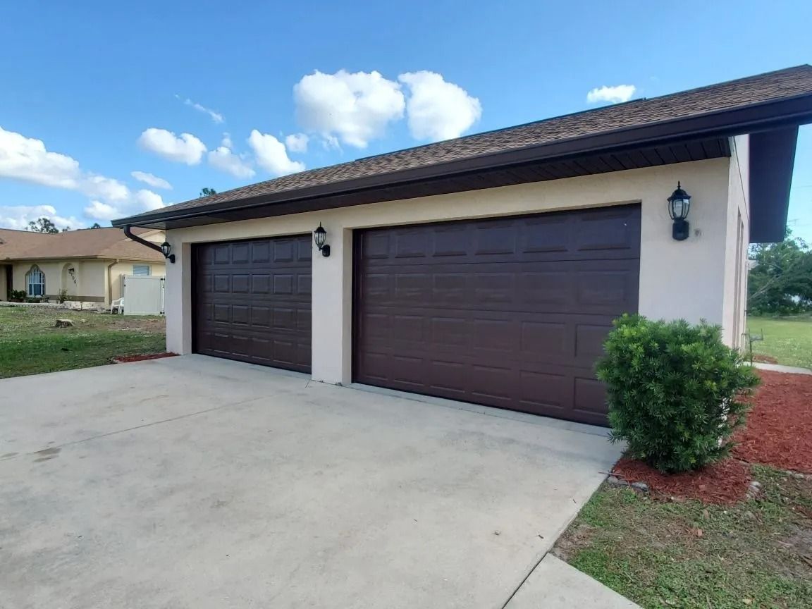 Two-car garage with brown doors, beige walls, and concrete driveway under a blue sky.