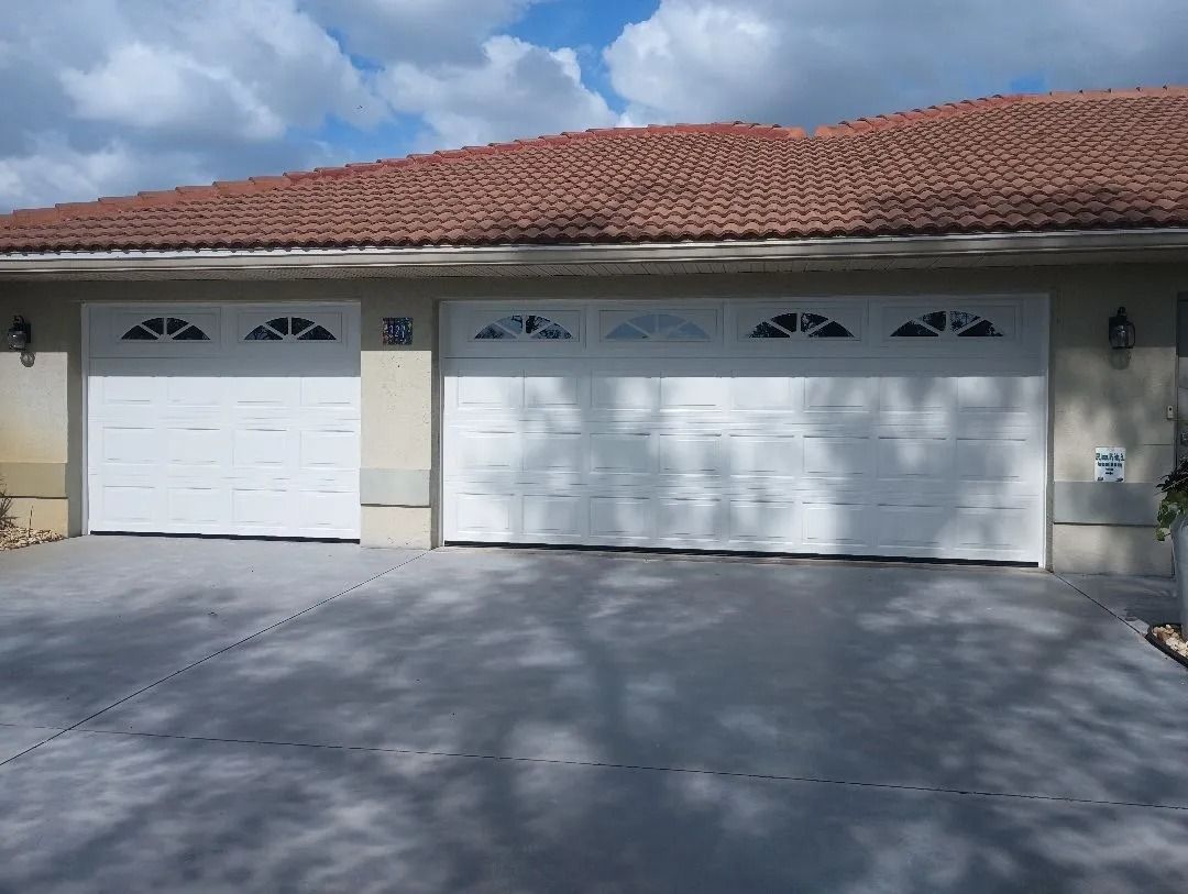 White garage doors with arched glass panels on a gray driveway under a red-tiled roof.
