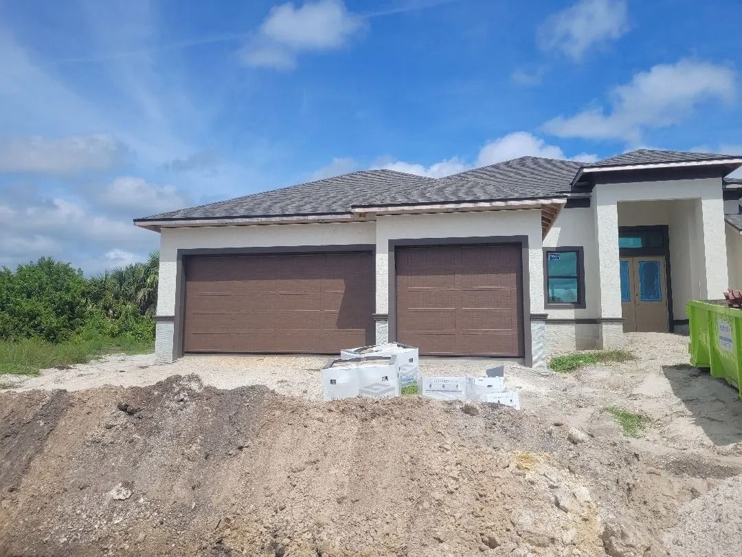 New house under construction with brown garage doors, gray roof, and blue sky.