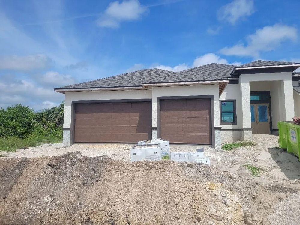 New house under construction with brown garage doors, gray roof, and blue sky.
