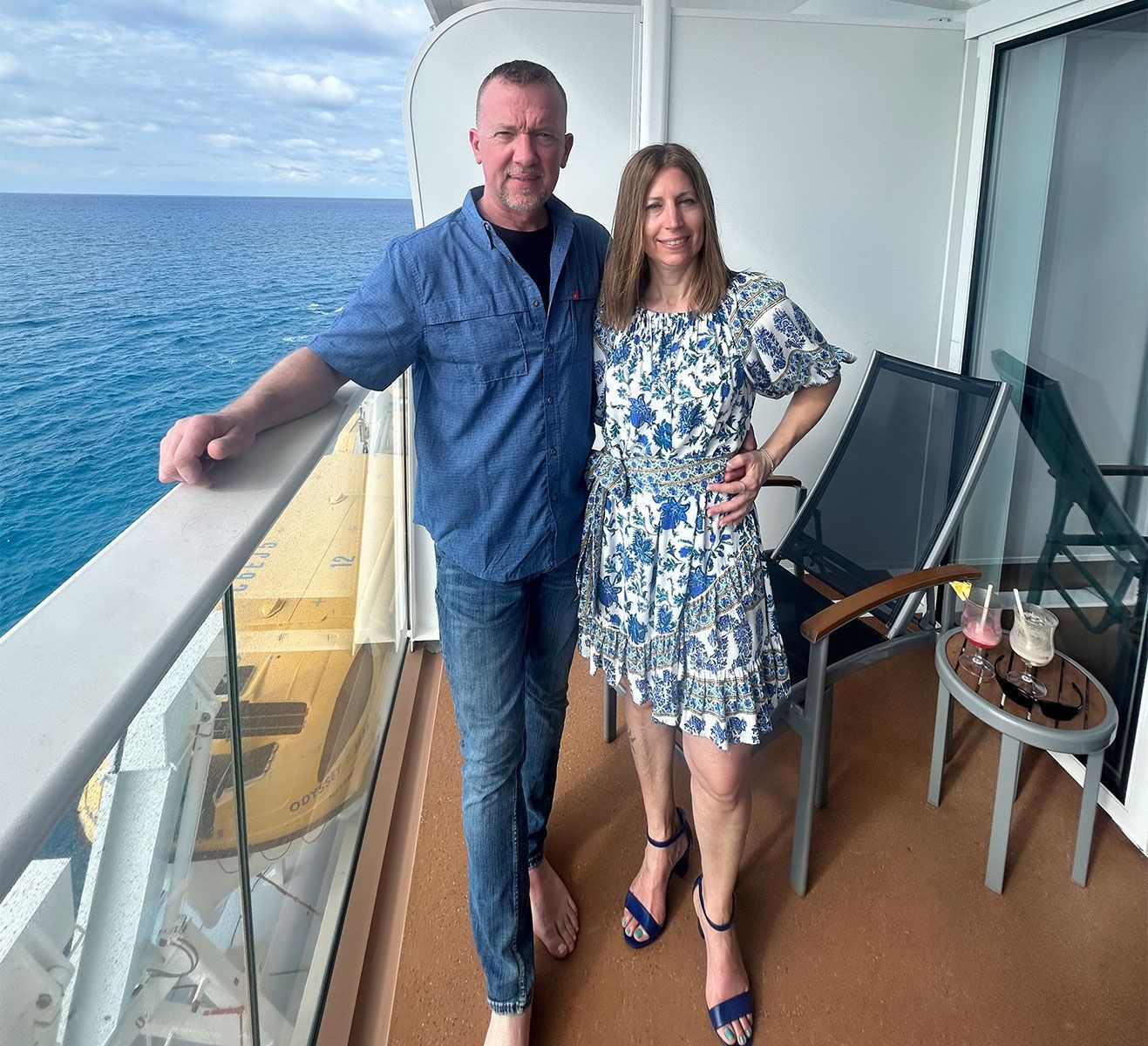 Couple on cruise ship balcony with ocean view, drinks on a side table.