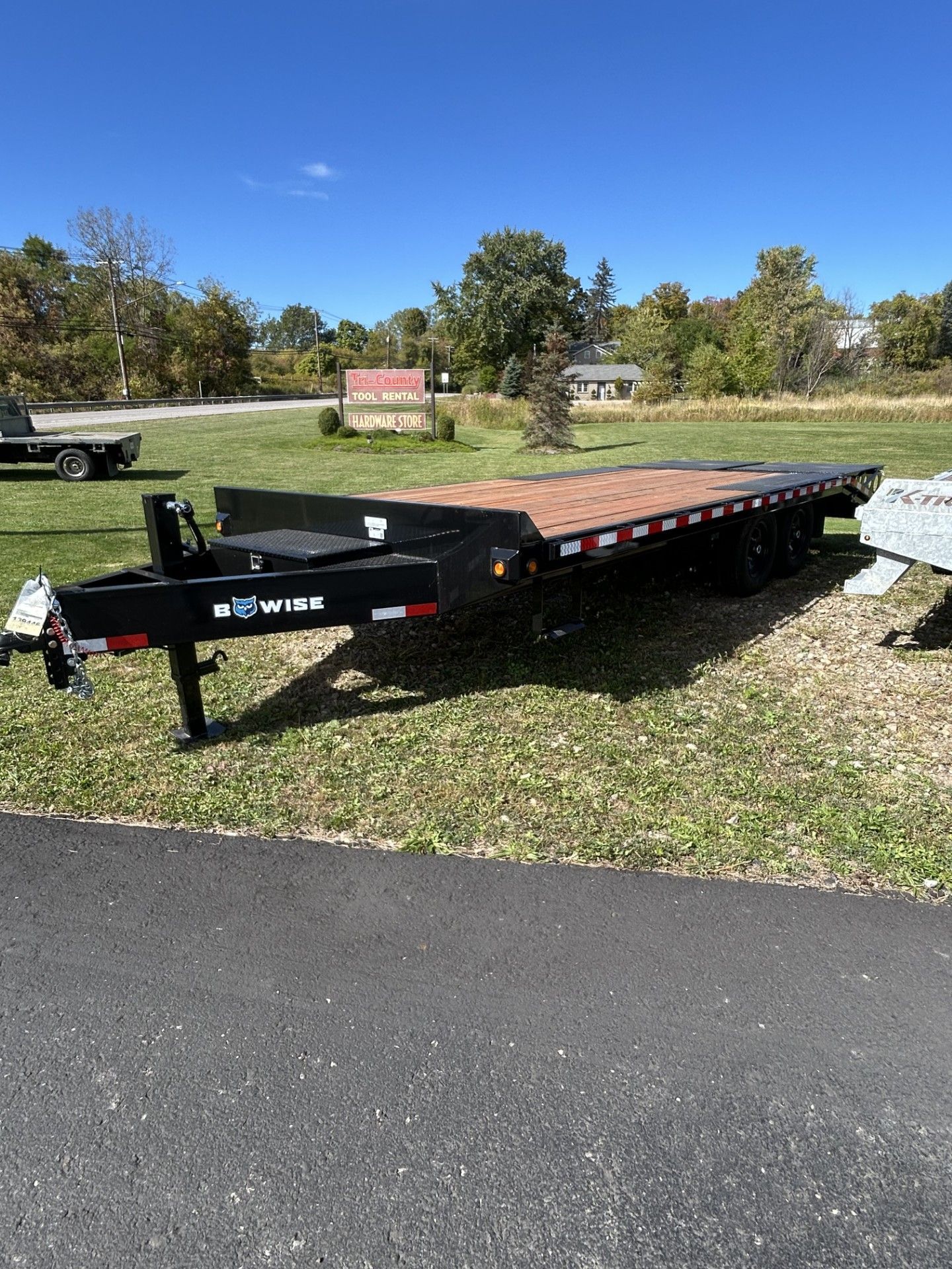 Black flatbed trailer on a grassy lot, under a blue sky.