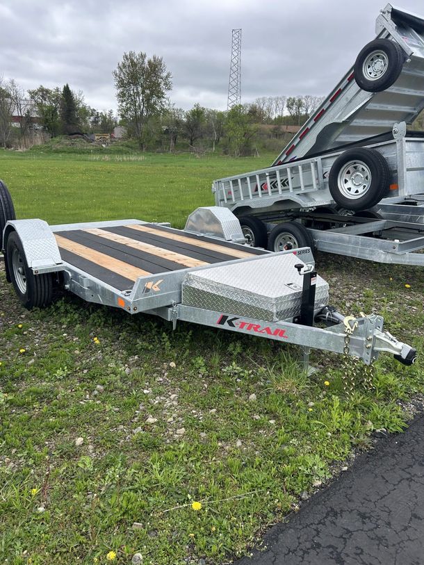 A silver and black trailer parked on grass; another trailer is behind it.