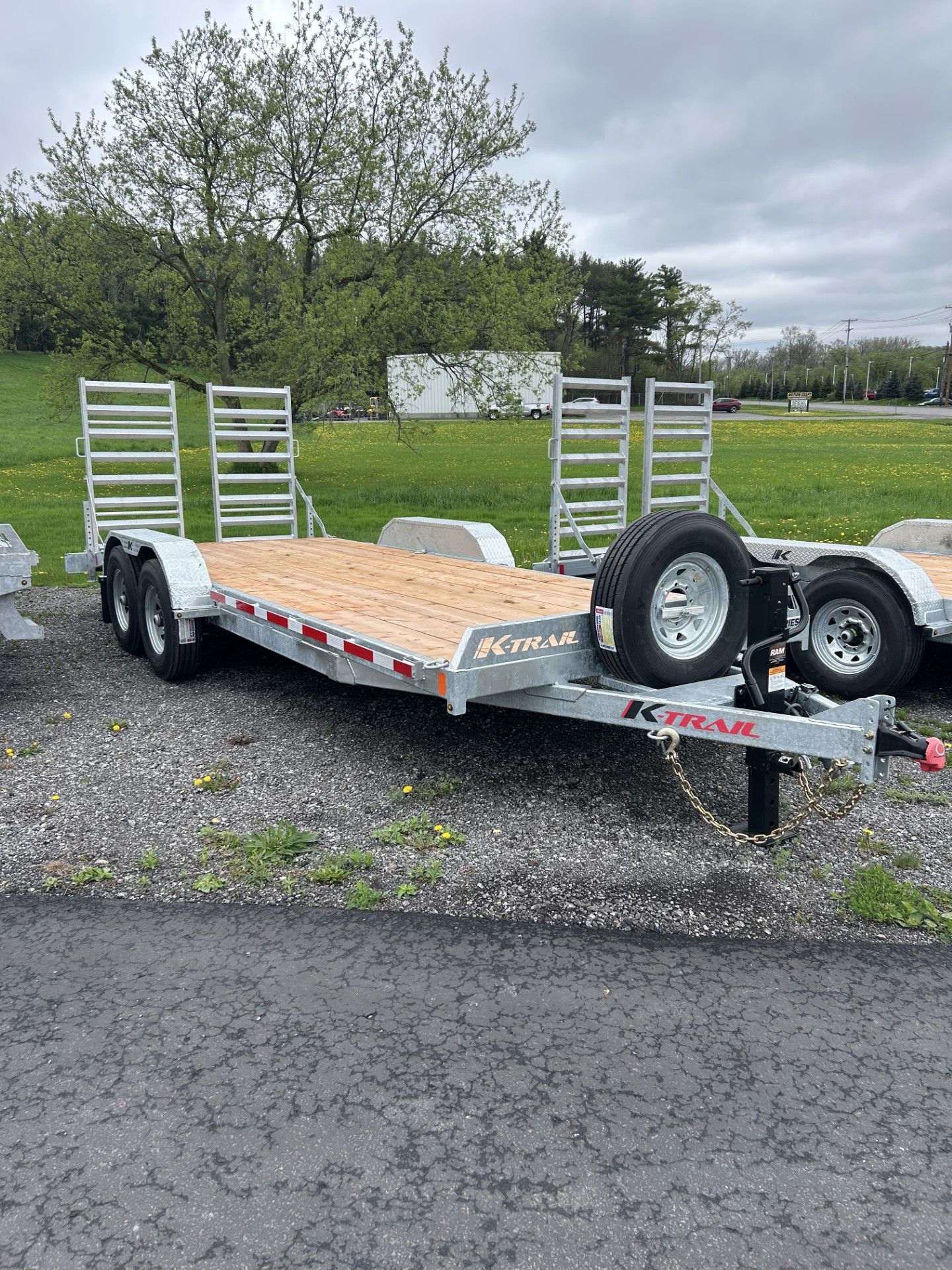 Flatbed trailer with wood deck and loading ramps, parked outside on a cloudy day.