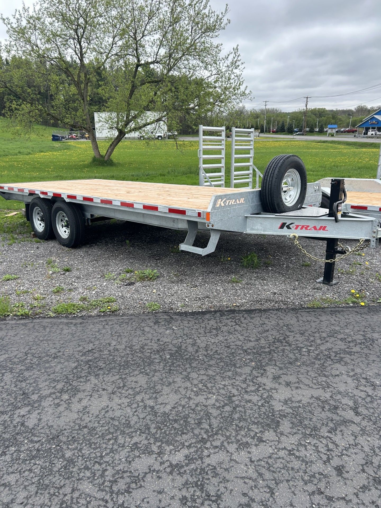 Flatbed trailer on a gravel surface with a spare tire mounted.