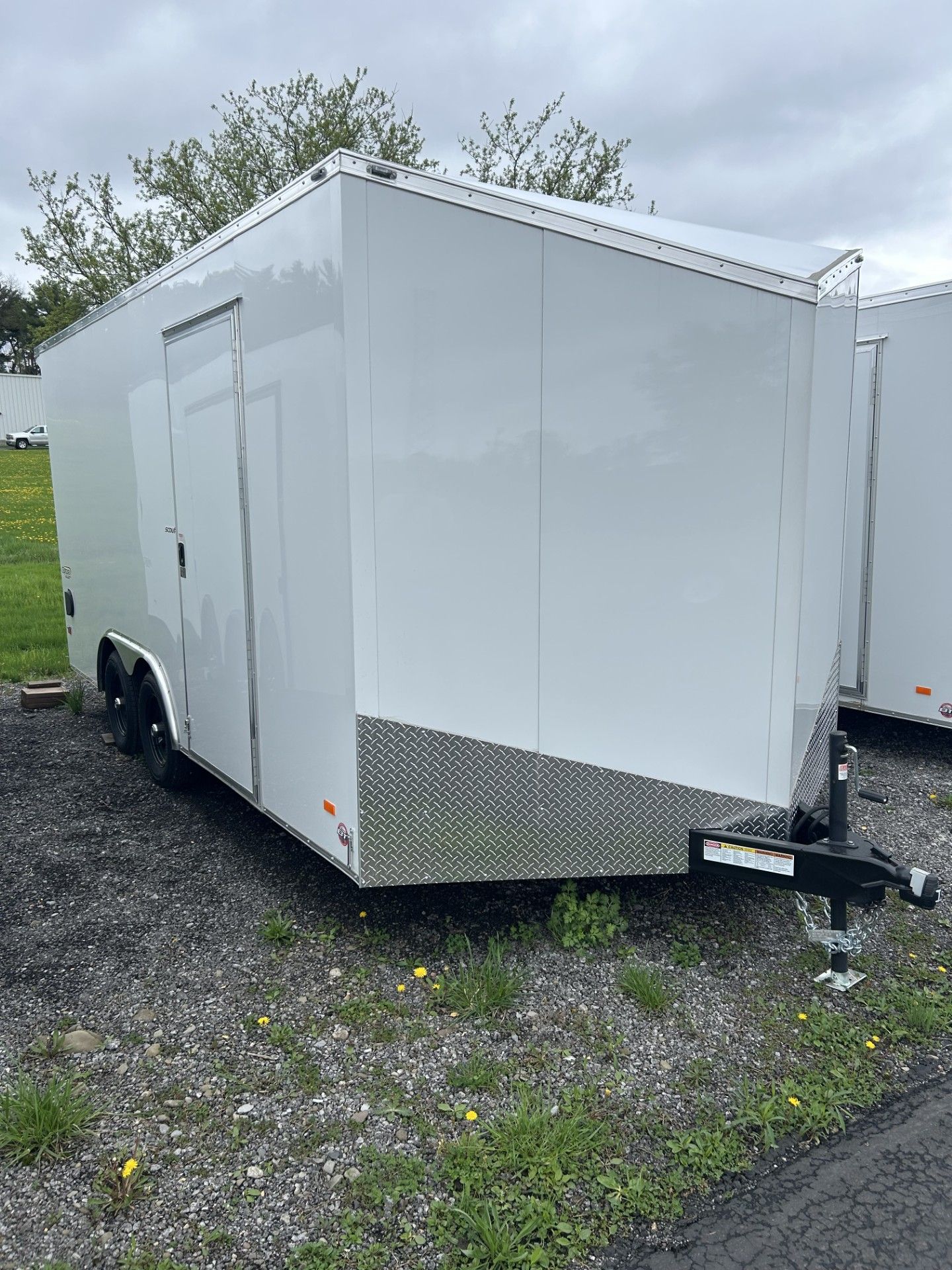 White enclosed cargo trailer on gravel with a door, angled front.