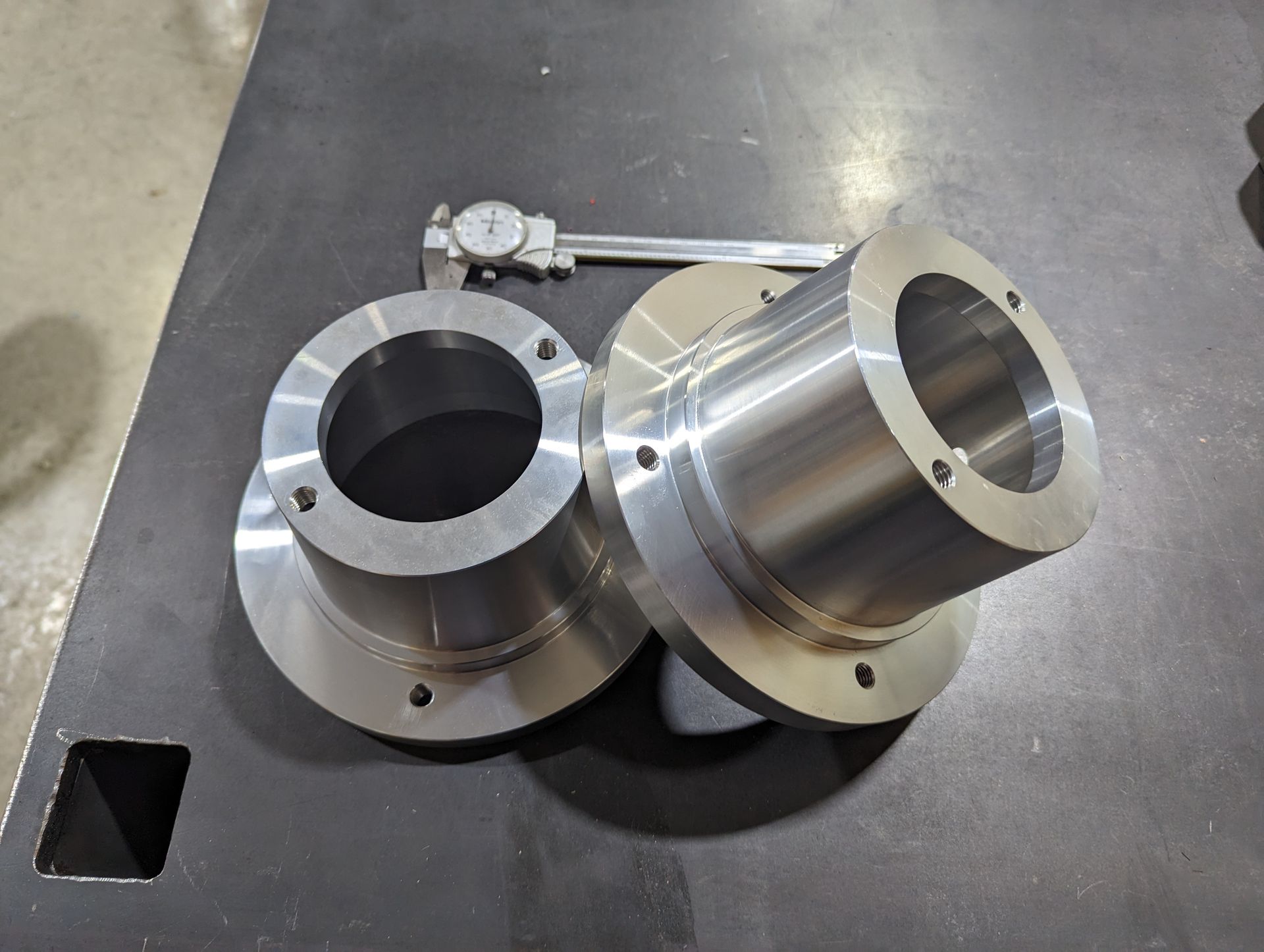 Two pieces of metal are sitting on a table next to a measuring device.