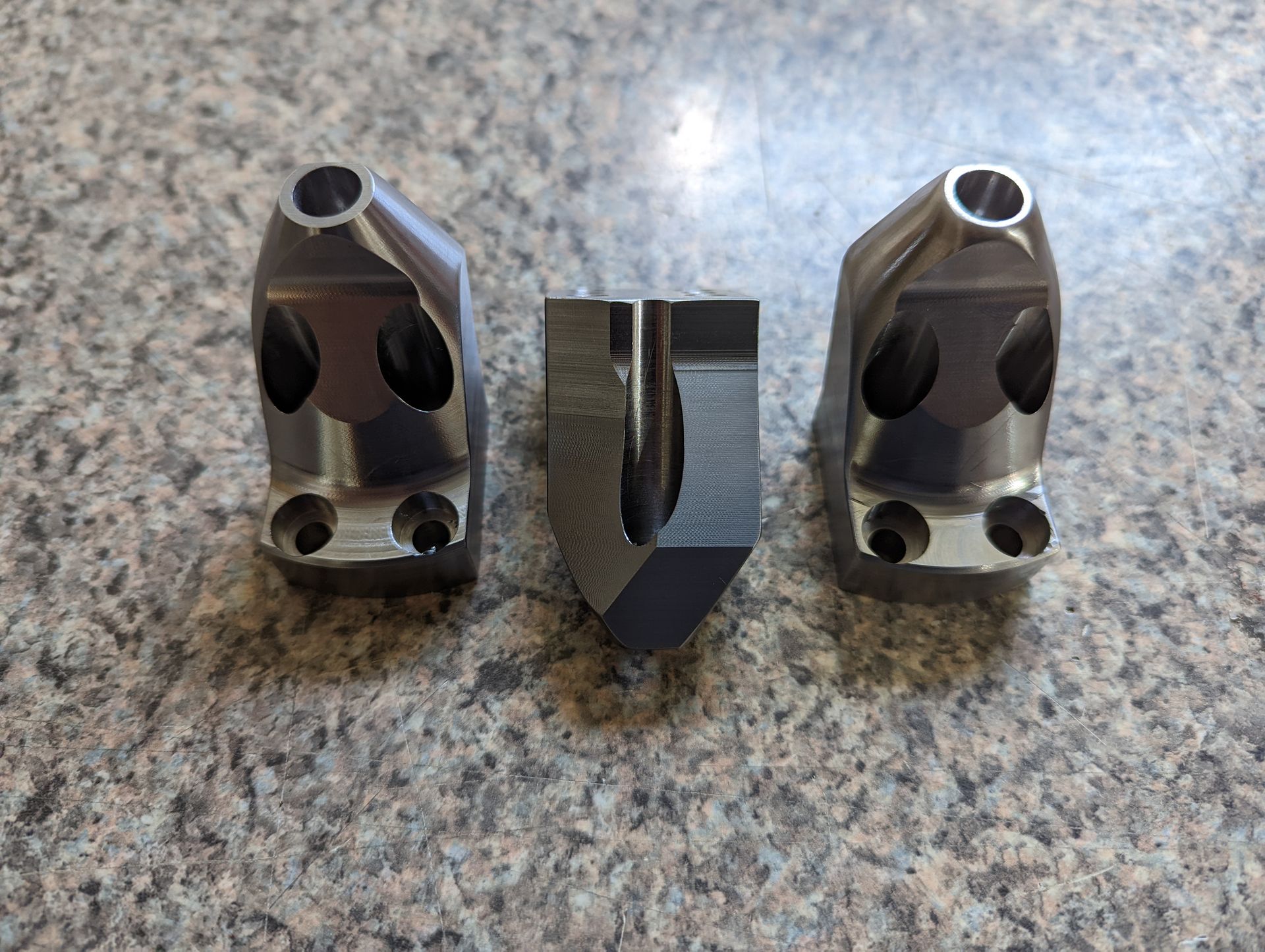 Three metal pieces are sitting on a granite counter top.