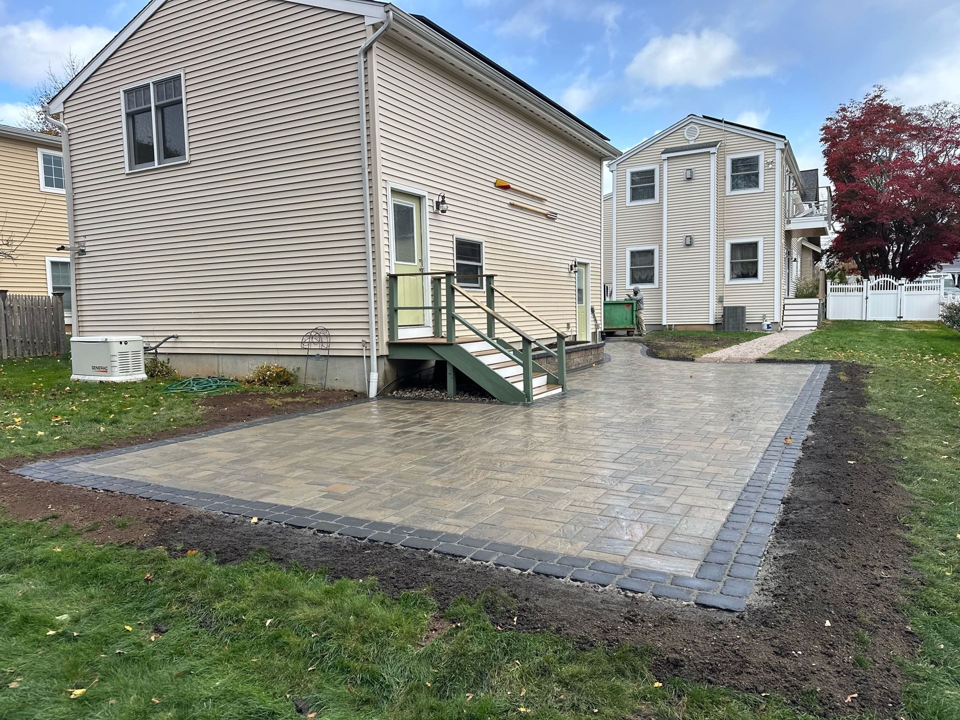 Backyard patio with gray pavers bordered by darker pavers, near houses and grass.