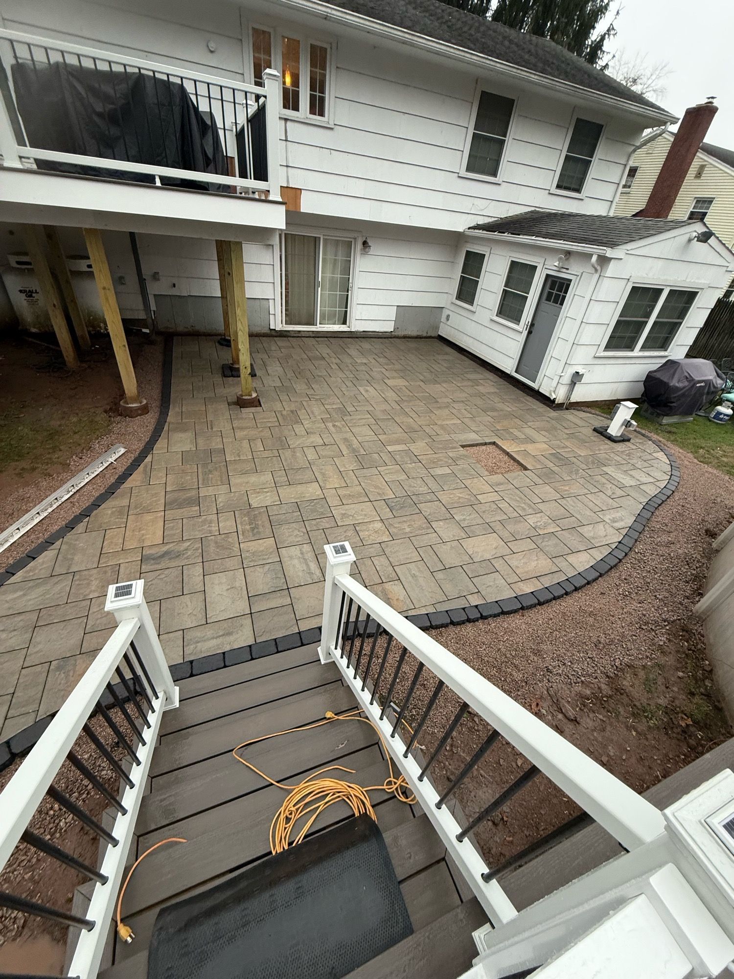 Backyard patio with paved area, stairs, house, and outbuilding.
