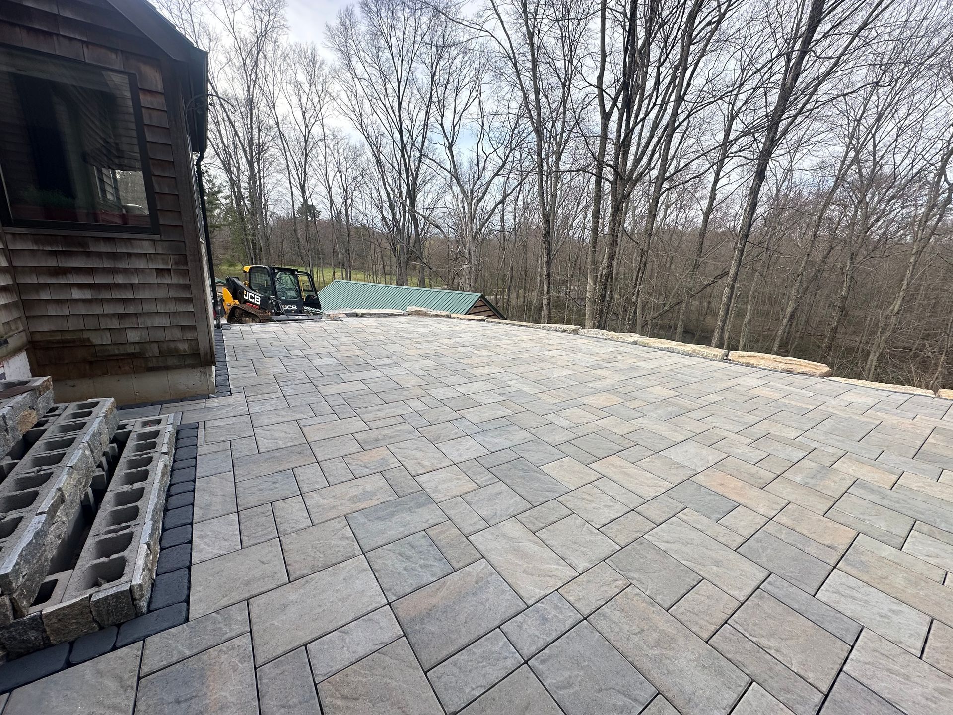 Newly paved patio with gray pavers next to a wooden building and trees.