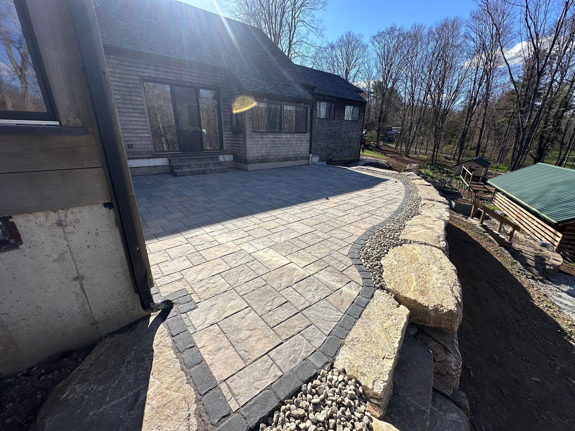 Brick patio and path alongside a rustic wooden building and a small log cabin, surrounded by trees.