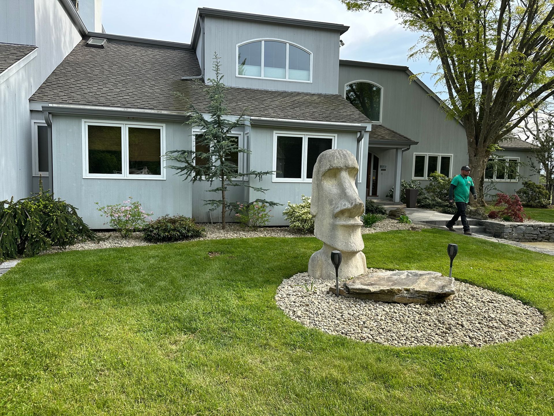 Gray house with a front yard. Statue, man, green grass.