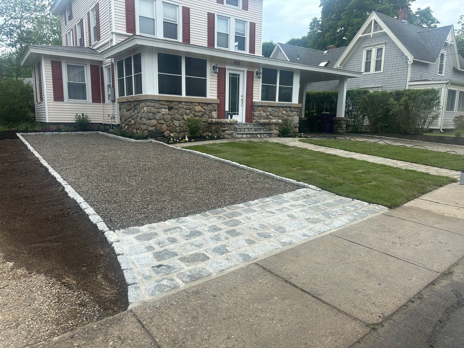 A house with stone foundation, gravel and paved driveway. Freshly laid grass.