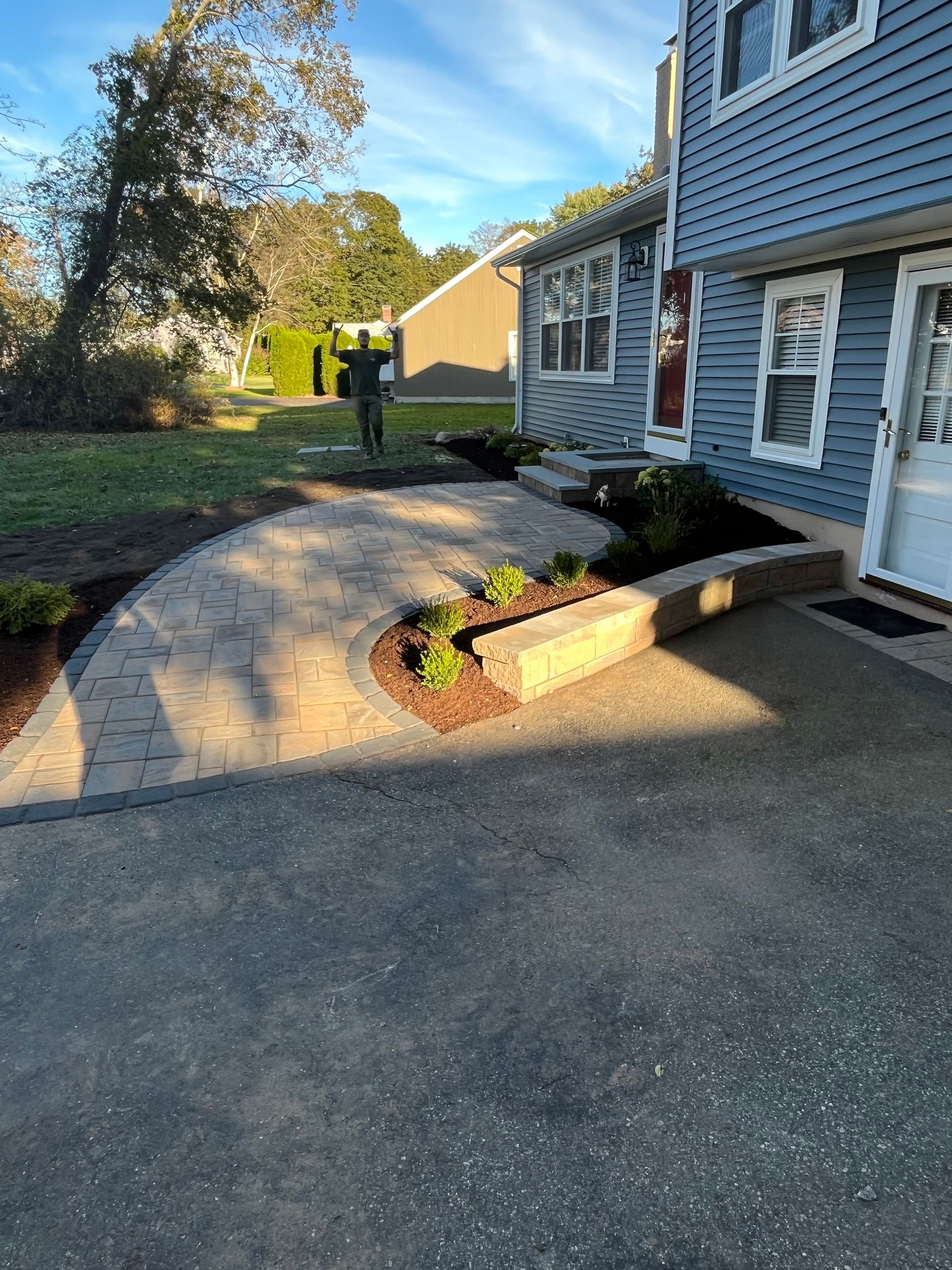 Pathway leading to a blue house with landscaping, a stone retaining wall and flowers.