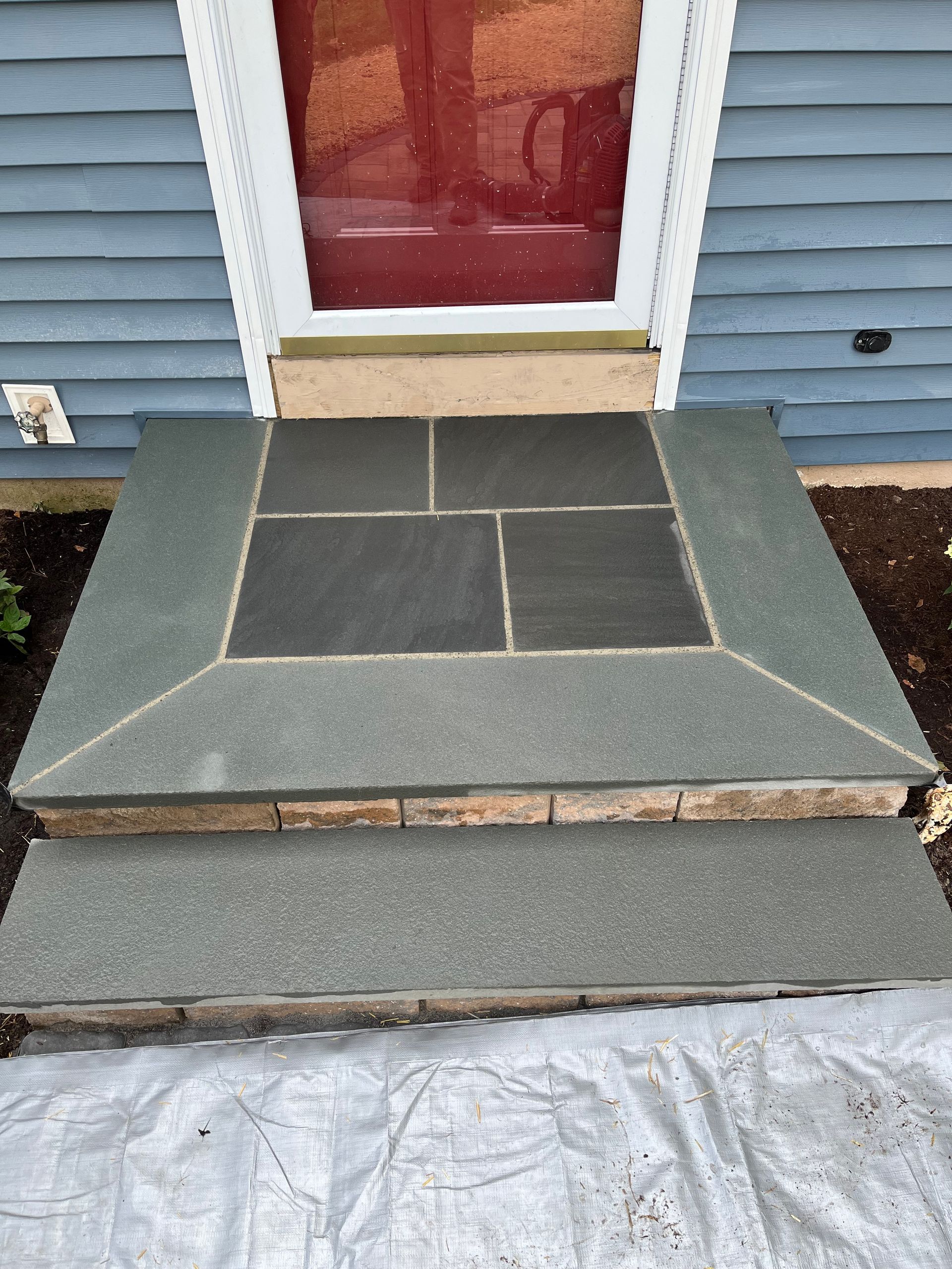 Stone entrance steps to a house with a blue exterior and a red door.