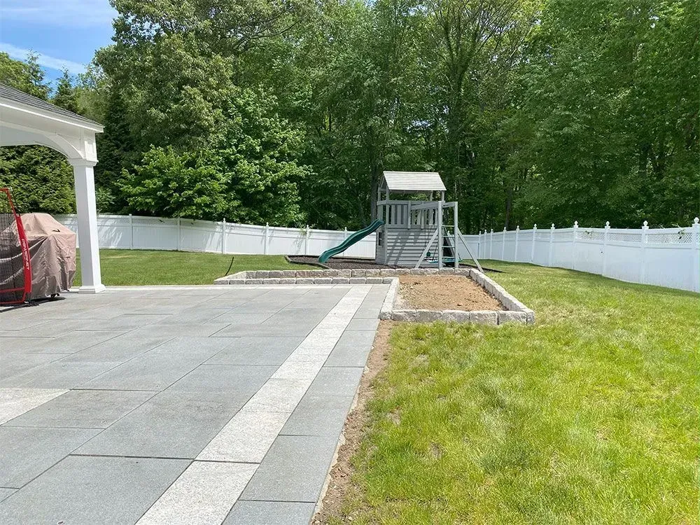 A backyard with a playground, white fence, and patio.