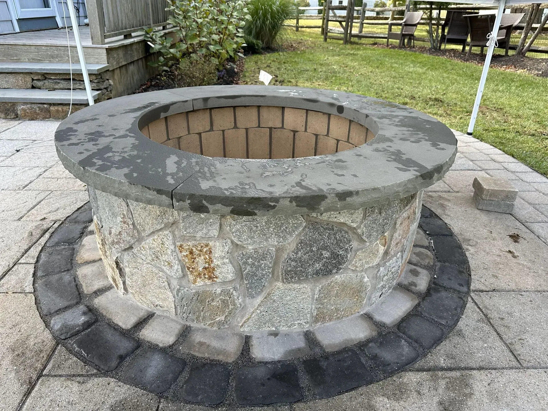 Stone fire pit on a stone patio with a grassy background.