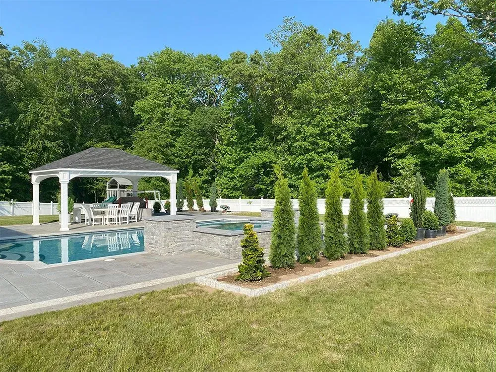 Gazebo and pool in a backyard, surrounded by trees and greenery on a sunny day.