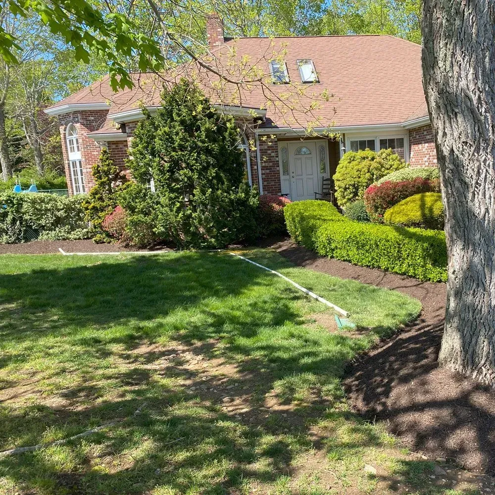 House with red brick facade, green lawn, trimmed hedges, and brown roof.