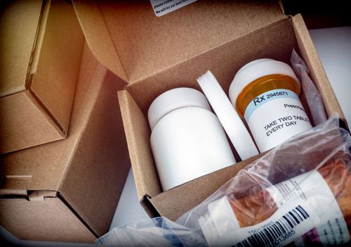 Open cardboard box with white pill bottles and a sealed medicine package.
