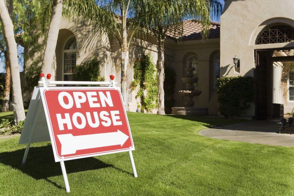 Red open house sign on a lawn in front of a house with palm trees.