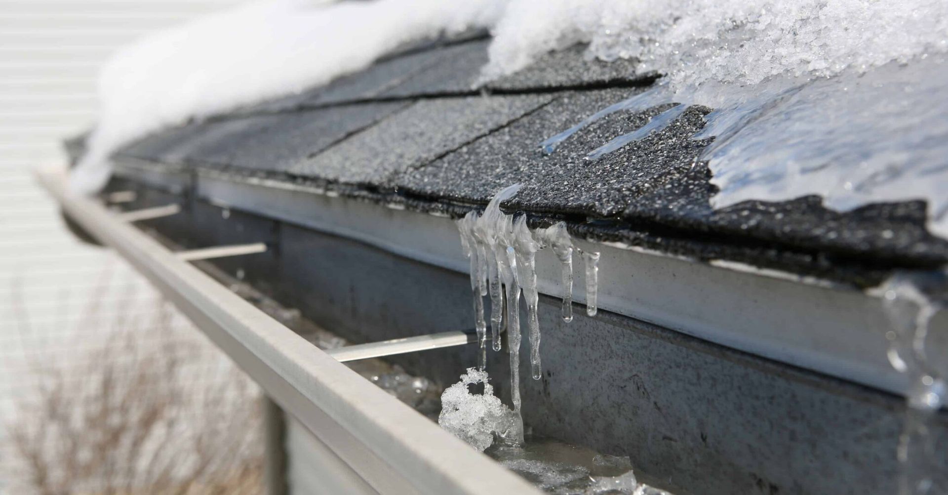 Snow and ice on a roof's edge with a gutter; icicles hang down.
