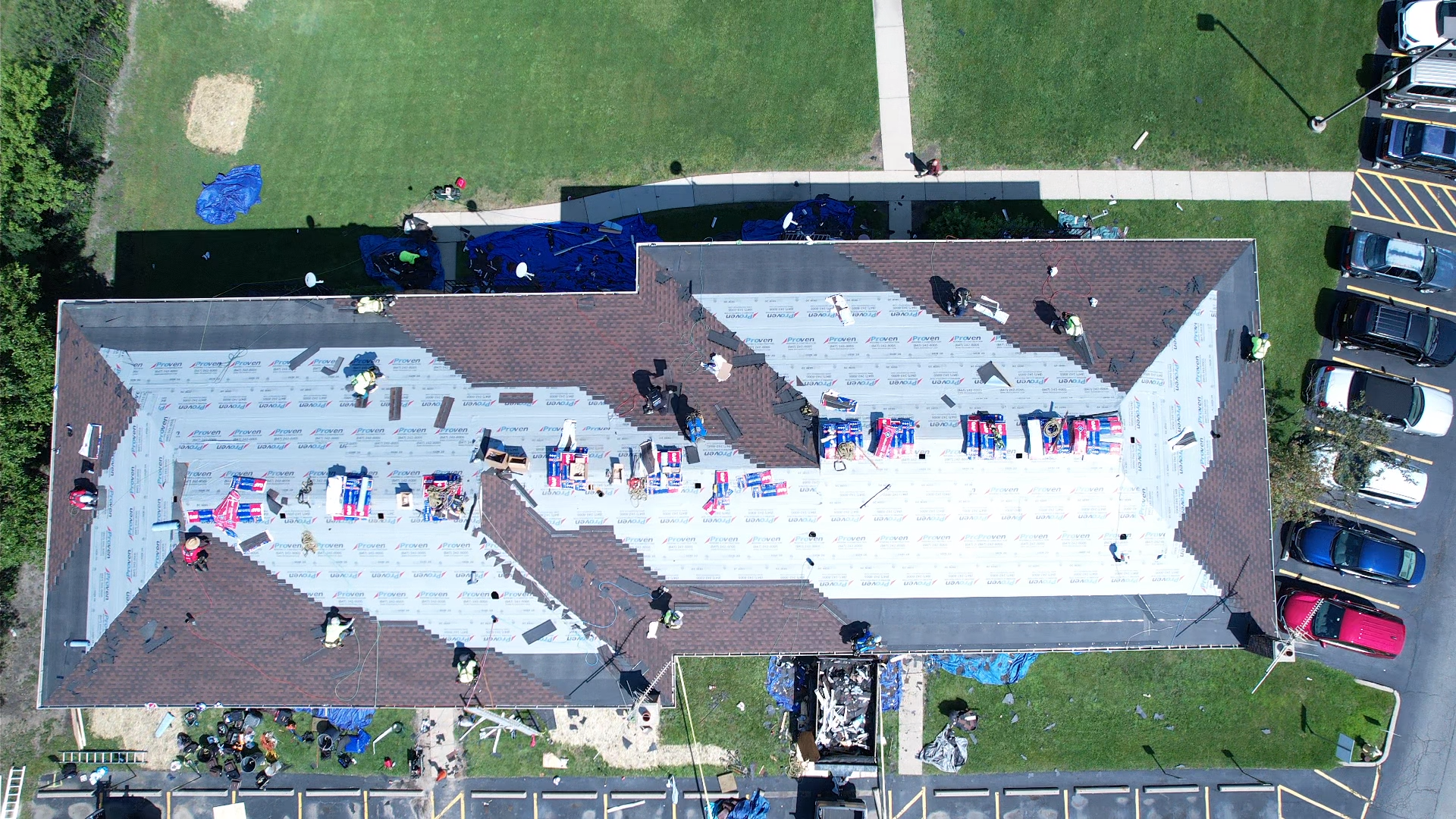 Aerial view of a building roof under repair with tarps and workers.