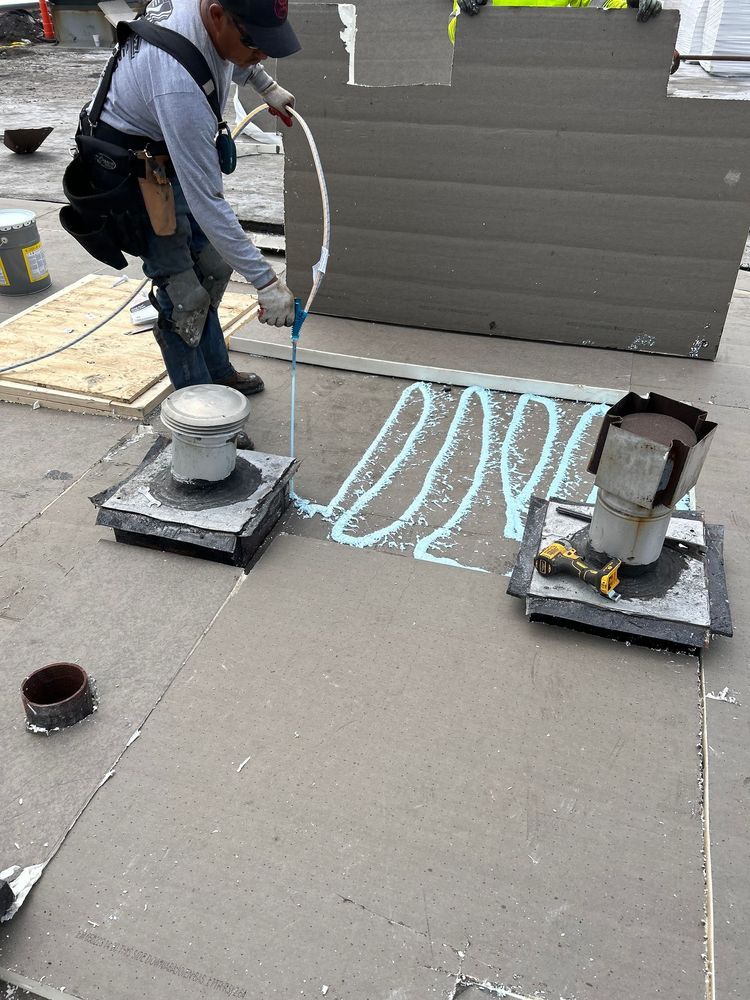 Roofer applying sealant to a flat roof around vents, using a caulking gun.
