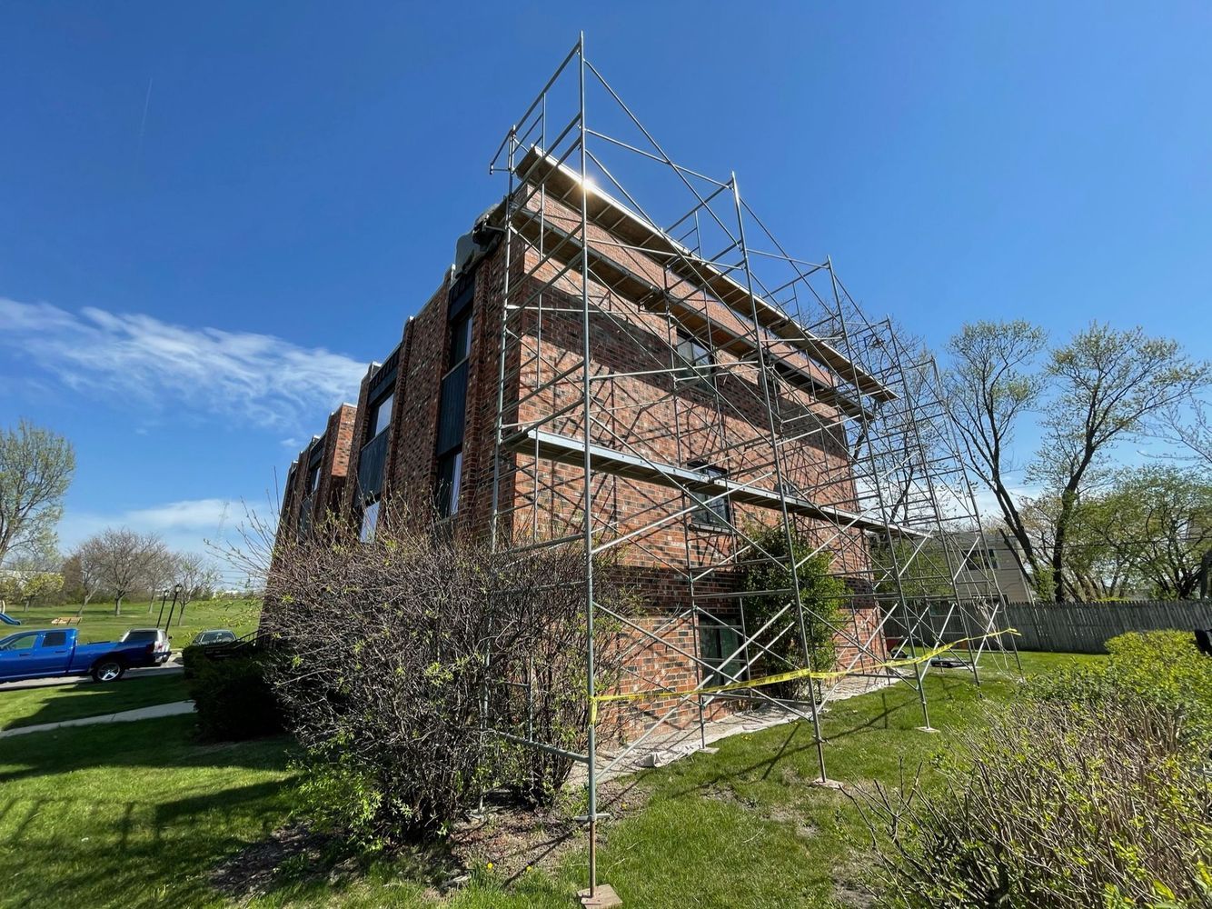 Brick building with scaffolding on the side, set on a grassy hill with blue sky.