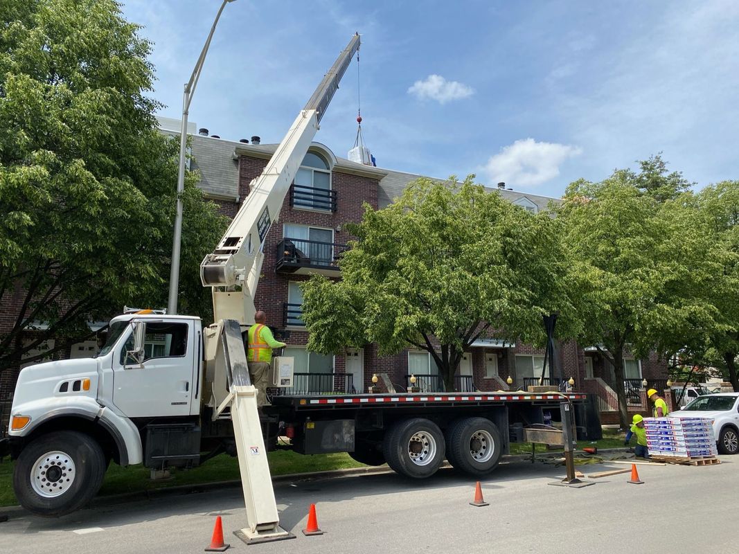 Truck with crane lifting materials to a building roof; two workers in safety vests.