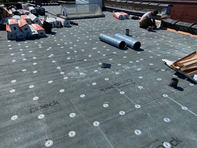 Rooftop with installed membrane, worker, and materials. Gray roofing, white fasteners, and stacked components.