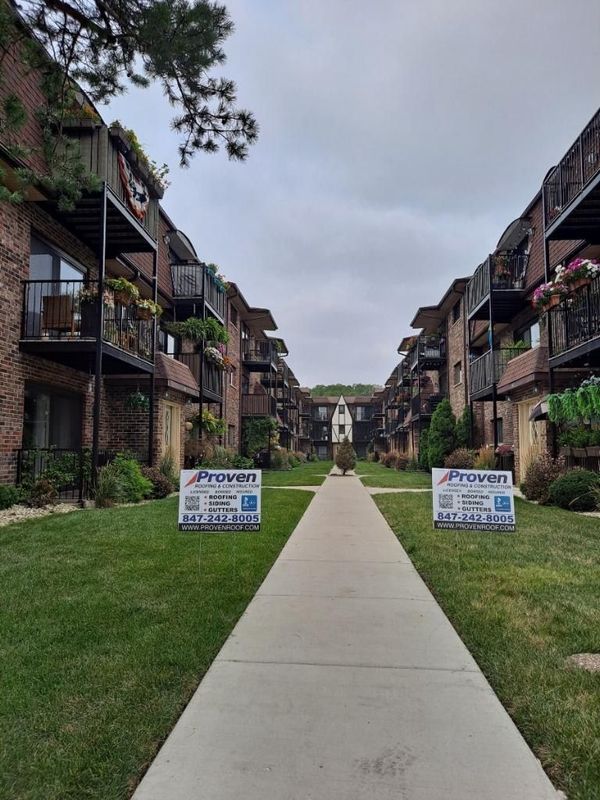Apartment buildings with balconies, a walkway, and green lawn; signs posted on either side of the walkway.