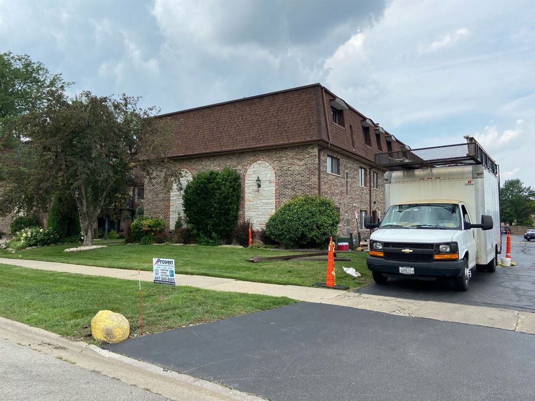 A two-story brick building with a moving truck parked in front, orange cones and a sign on the lawn.