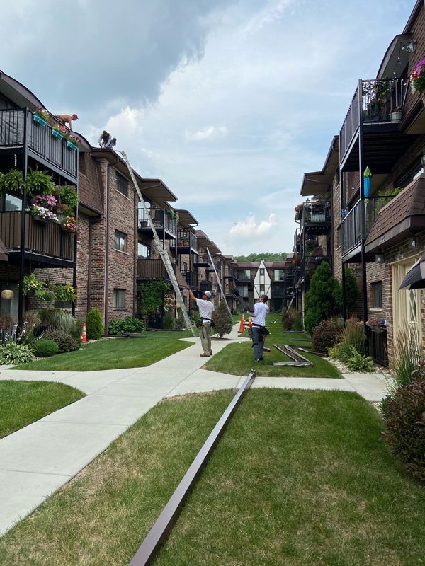 Workers with ladders installing on the roof of an apartment building, grass and walkway in foreground.