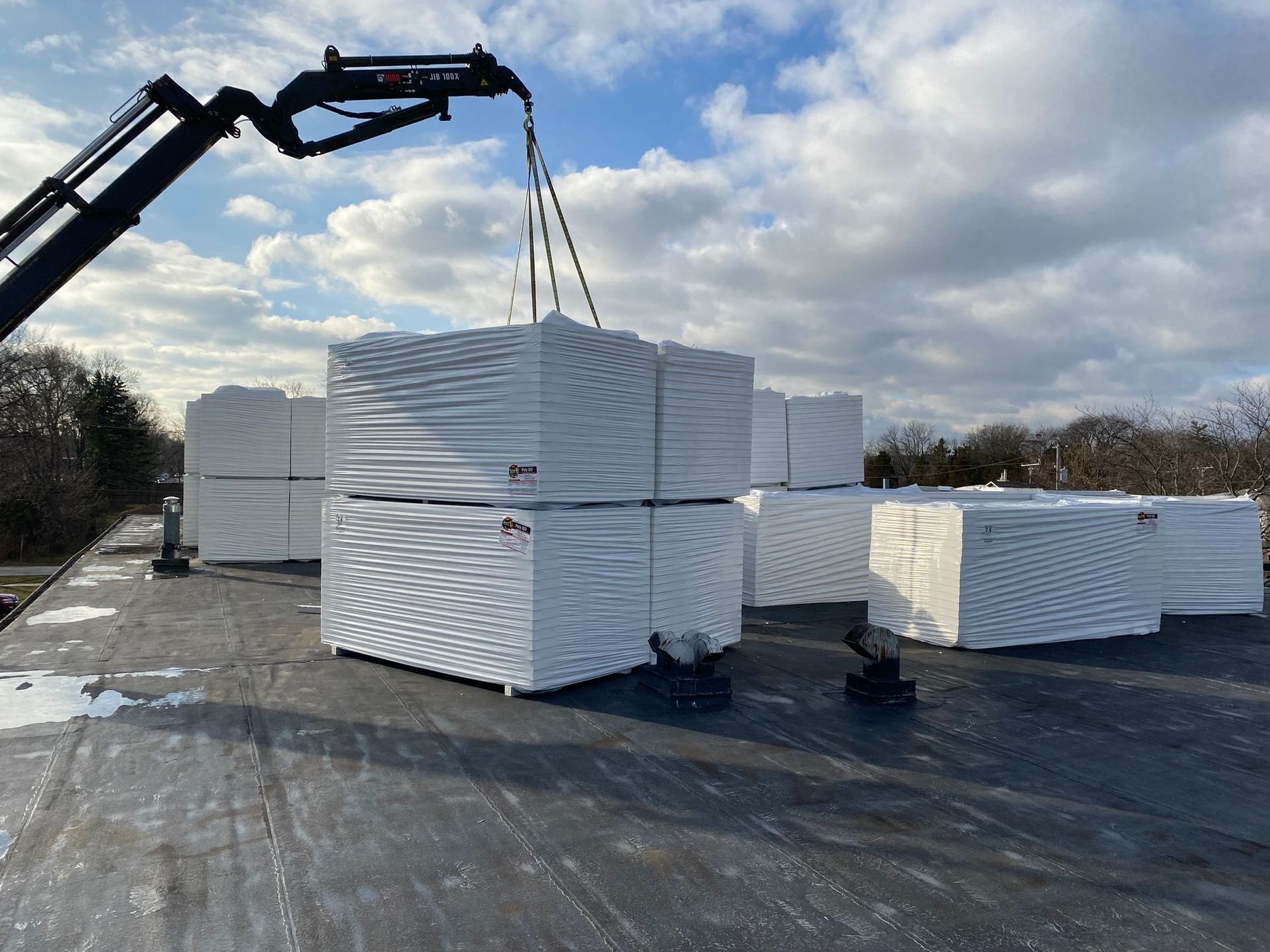 Crane lifting wrapped bundles of white material onto a flat surface under a cloudy sky.